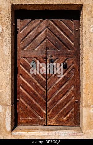 Weathered wooden door with herringbone planks, metal knocker and latch, rustic architectural detail in warm light, vertical image Stock Photo