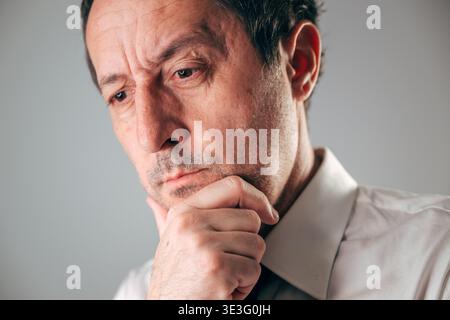 Pensive businessman, hand on chin deep in thought, selective focus Stock Photo