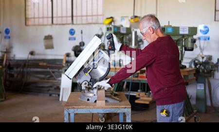 Senior carpenter cutting wood using miter saw in workshop Stock Photo