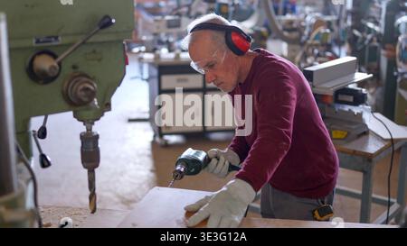 Senior carpenter drilling wood plank in workshop Stock Photo