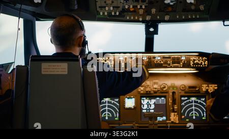 Male airline captain fixing altitude and longitude buttons, using dashboard navigation command and control panel. Flying airplane with aircrew and radar compass, power engine and windscreen. Stock Photo