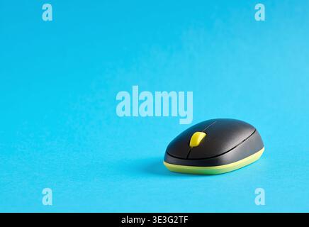 Modern wireless computer mouse with yellow scroll wheel on a bright blue background, representing technology and connectivity Stock Photo