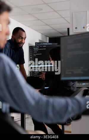 Multi ethnic team of software developers talking about html code in it company office. Artificial intelligence cloud programers compiling algorithms on terminal window server, doing teamwork Stock Photo