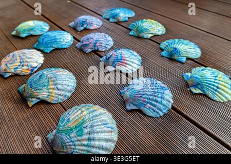 Colorful seashells scattered on weathered wooden planks. Shells display vibrant, swirling patterns in blues, greens, and yellows Stock Photo