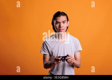 Teenager playing video games with joystick, entertainment activity. Concentrated young asian man holding gamer gadget, person using console wireless controller, enjoying videogames Stock Photo