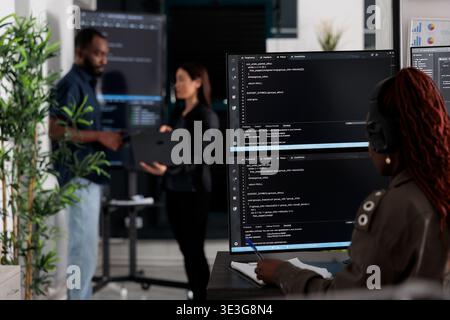 Multi ethnic team of software developers analyzing code on wall screen tv, using digital device and working with artficial intelligence. Programmers parsing cloud computing project with big data. Stock Photo