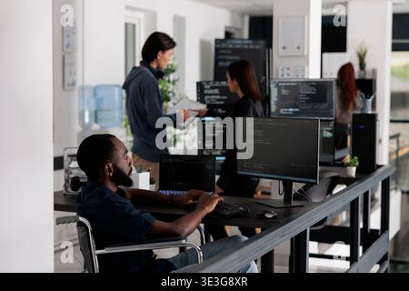 Disabled african american it engineer working on server program with computer, typing html code in coding office. web developer with chronic disability writing script with system algorithms. Stock Photo