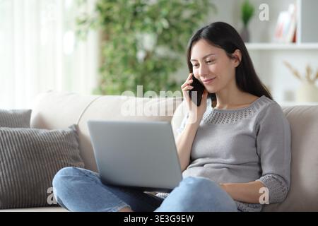Satisfied asian woman making phone call about online content sitting on a couch at home Stock Photo
