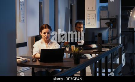 Portrait of confident happy manager working on laptop to plan report, doing research presentation late at night. Using web software to create financial project, app developer. Stock Photo
