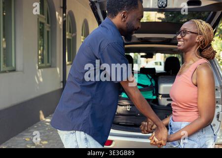 Romantic black people holding hands in excitement for their road trip, preparing for the holiday journey with packed car and road essentials. Couple in love travelling for relaxation. Stock Photo