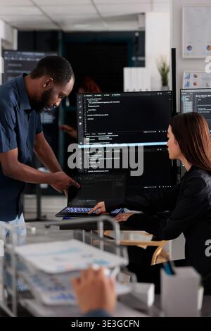 Diverse team of app developers talking about programming in software company office. Artificial intelligence cloud programers compiling code on terminal window server, doing teamwork Stock Photo