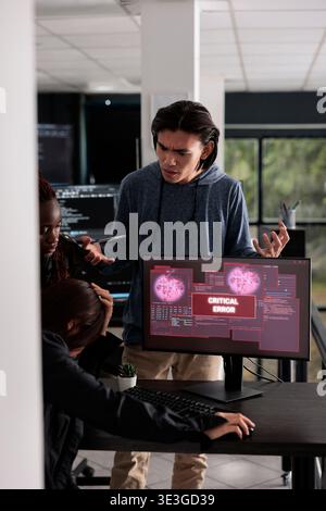 Multi ethnic team of it programmers having hacked server and security breach alert on pc display, trying to solve hacking problem. Encountering critical error message flashing on screen. Stock Photo