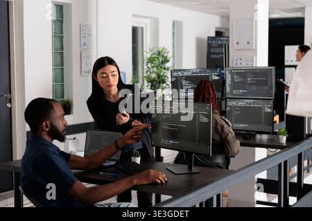 African american web developer using computer to write code and develop algorithm program in big data office room. System engineers working on user interface with html script and terminal window. Stock Photo