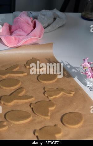In a kitchen, a baking sheet holds shaped gingerbread cookies ready to be decorated. Easter bunny and other symbols stand out, reflecting the spirit of the holiday. Stock Photo