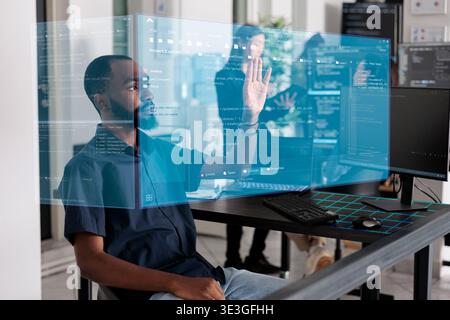 African american programmer working with hologram checking data while creating security system. Using holographic image and new interface for cloud computing, database code programming. Stock Photo