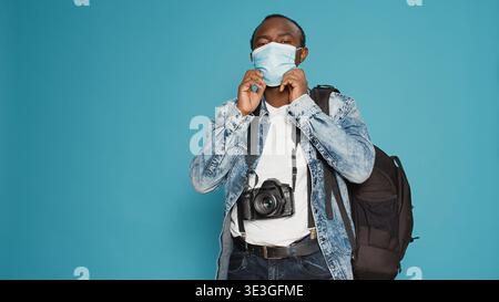 Adult photographer putting face mask on to leave on vacation trip, using camera to take pictures and capture urban adventure during covid 19 pandemic. Taking photos with equipment. Stock Photo