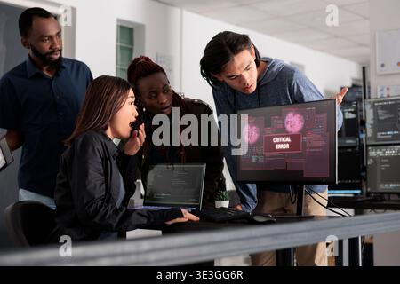 Team of software developers having web server hacked, reading critical error on computer display in agency. Multi ethnic programmers trying to solve hacking problem, firewall security. Stock Photo