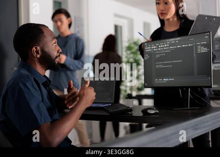 Diverse group of web developers analyzing html code and comparing data script in big data office room. Cloud programers working on system interface algorithm in development company. Stock Photo