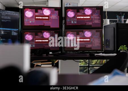 Empty data office desk with multiple programming computers flashing security breach warning on network app. Monitors displaying critical error message showing on screen with system crash alert. Stock Photo