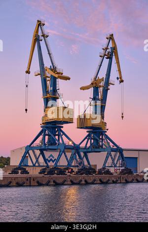 Wismar, Germany - 25 September 2025: View of the harbor cranes standing tall against the pastel sky, their yellow bodies contrasting with the blue fra Stock Photo