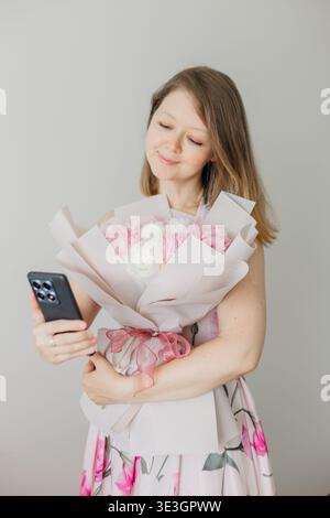 Young Woman holding bouquet of peonies taking smartphone selfie Stock Photo
