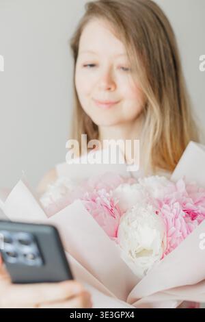 Young woman taking selfie with pink peonies bouquet Stock Photo