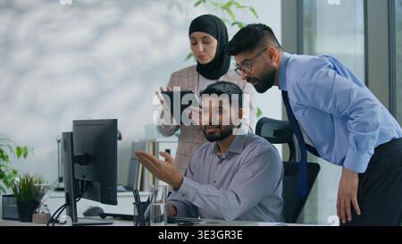 Arabian business man working with computer in office two colleagues come in Muslim businesswoman secretary with Indian boss leader check work online Stock Photo