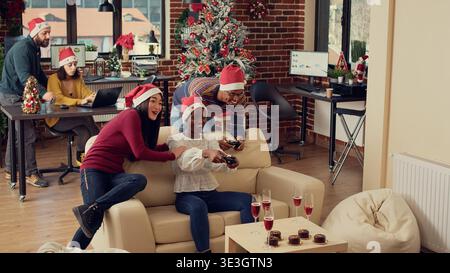 Cheerful colleagues playing video games at christmas party in office, feeling happy and enjoying winter holiday celebration. Using controllers on console to play gaming competition at festivity. Stock Photo