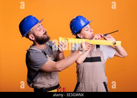 Contractors holding screwdriver and water level tool in studio shot, using ruler or leveler to work on renovation. Team of building experts being confident with renovating tools. Stock Photo