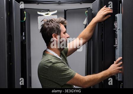 An IT technician adjusts equipment inside a server rack in a data center, checking connections and performing routine hardware maintenance to ensure network reliability, uptime and proper equipment operation. || Model released Stock Photo