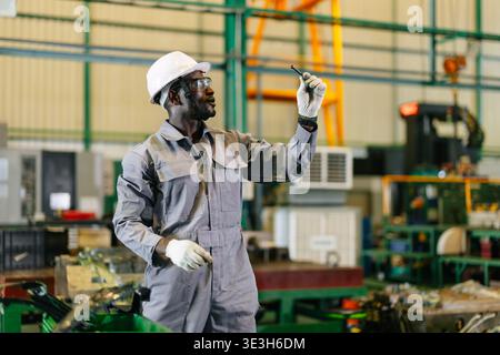 African Black male worker working check quality of metal part production in heavy industry factory with safety hard hat glove and protective glasses Stock Photo