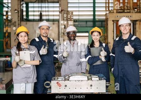 Group of professional success workers in safety uniforms stand together happy smiling in heavy industry factory. Stock Photo
