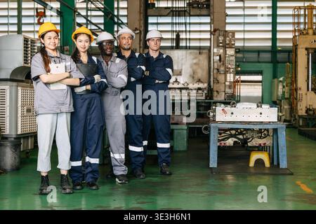 Group of professional success workers in safety uniforms stand together happy smiling in heavy industry factory. Stock Photo