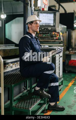 Professional Caucasian young German engineer male worker standing happy smiling in metal factory, vertical shot Stock Photo