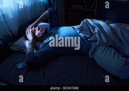 Adult Man Lying in Bed Suffering from Insomnia at Night Stock Photo