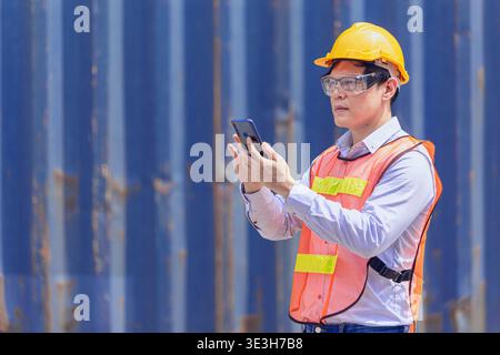Professional Asian man worker in port cargo shipping industry using smartphone technology device for work Stock Photo