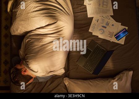 Young Man Sleeping in Bed Surrounded by Laptop and Documents Stock Photo