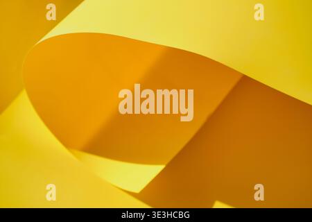 Yellow paper flowing with curves, shapes and shadows creating minimalist background Stock Photo