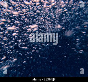 Air bubbles rise underwater in deep blue water creating an abstract background as seen from beneath the surface Stock Photo