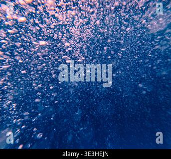 Bubbles rising in deep blue water with light filtering through, creating a textured underwater effect. Stock Photo