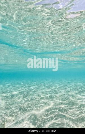 Clear shallow water view from underwater, with gentle ripples and sunlight creating patterns on the sand below. Stock Photo