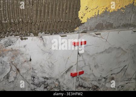 Close-Up of Tiling Process Featuring Marble and Gold Finishes with Red Spacers for Alignment Stock Photo