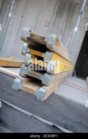 A careful stack of wooden and yellow construction formwork beams rests against a textured concrete wall on an active building site. Stock Photo