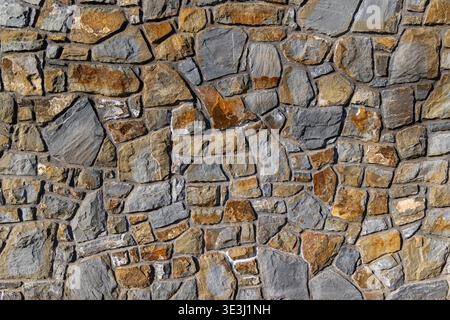 Gray and Brown Stone Wall Texture. Full frame view of an irregular gray and brown stone wall with mortar joints, showing rustic masonry texture and Stock Photo