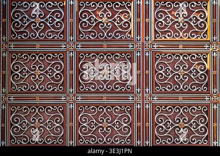 Ornate Wrought Iron Gate Pattern Background. Close-up of an ornate wrought iron gate with repeating floral scrollwork, rich red tones, and symmetrical Stock Photo