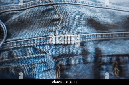 Macro shot of faded blue denim fabric showcasing texture, seams, and orange thread stitching Stock Photo