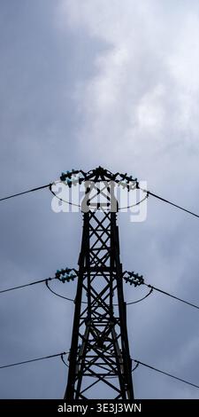 Low angle view of electric transmission tower silhouette with power lines against cloudy sky, representing energy infrastructure and electricity distr Stock Photo