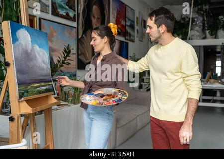 Smiling painters spouses works on painting. Happy woman artist with husband at home studio workshop Stock Photo