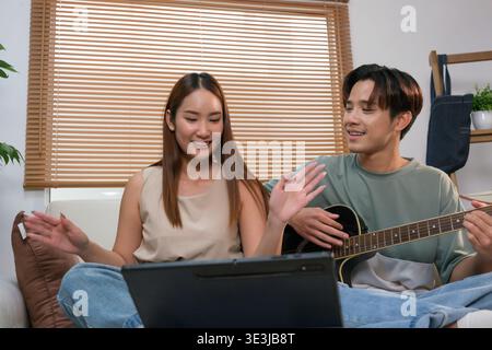 A young Asian couple spends their free time playing guitar and singing at home. Stock Photo
