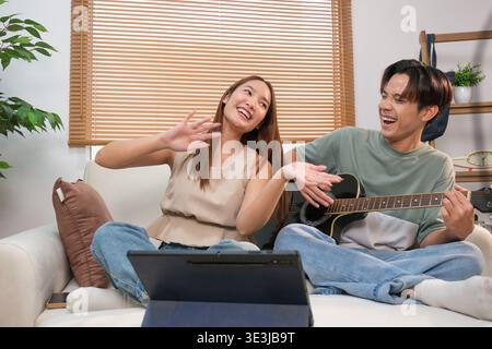 A young Asian couple spends their free time playing guitar and singing at home. Stock Photo